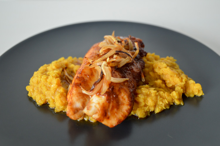 Cod and lentils topped with onions and cilantro served on a black plate