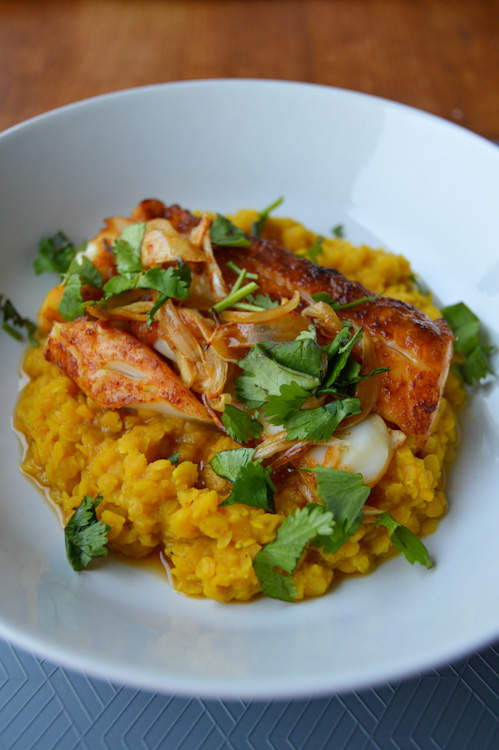 A white bowl with red curry cod and red curry lentils topped with onions and cilantro