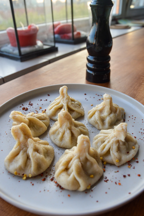 A plate of 7 khinkali (Georgian dumplings) sprinkled with red pepper flake and black pepper with a pepper grinder in the background