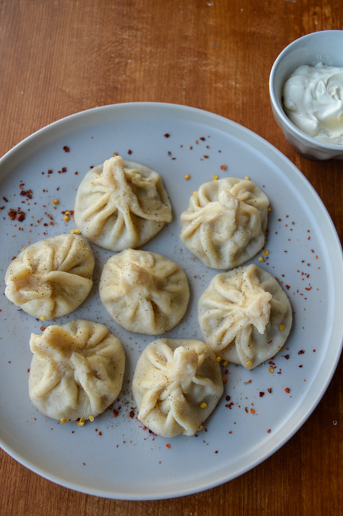 Grey plate of 7 khinkali (Georgian soup dumplings) served with a side of crème fraîche