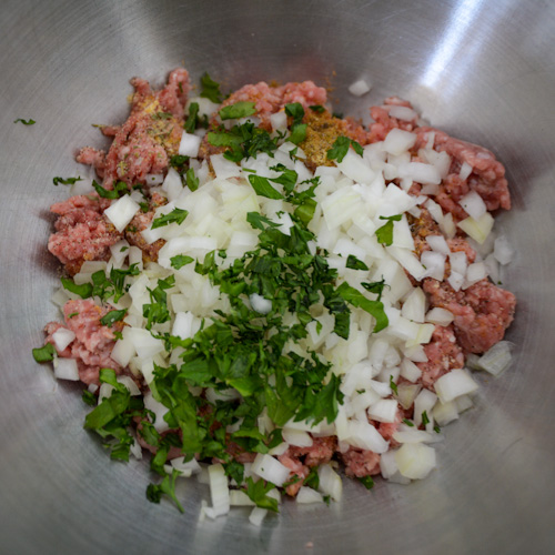 Ground lamb with chopped onion and green herbs in a metal bowl