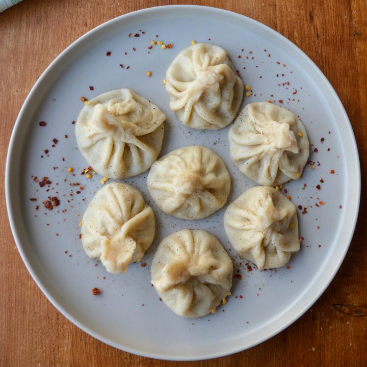 A grey plate with 7 khinkali sprinkled with red pepper flake