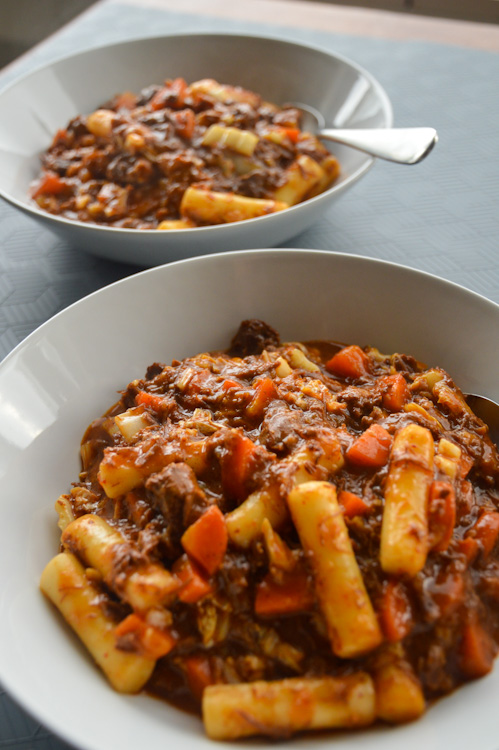 Two bowls of Korean beef stew with tubular rice cakes and carrots, one clear in the foreground, one a bit blurred in the background