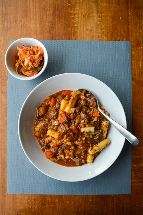 Two bowls: one of Korean beef stew with rice cakes and a smaller bowl with a side of kimchi