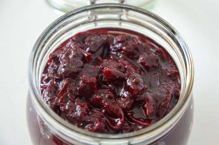 Glass jar with a lid (most of which is out of the frame) full of delicious cooked plum onion chutney