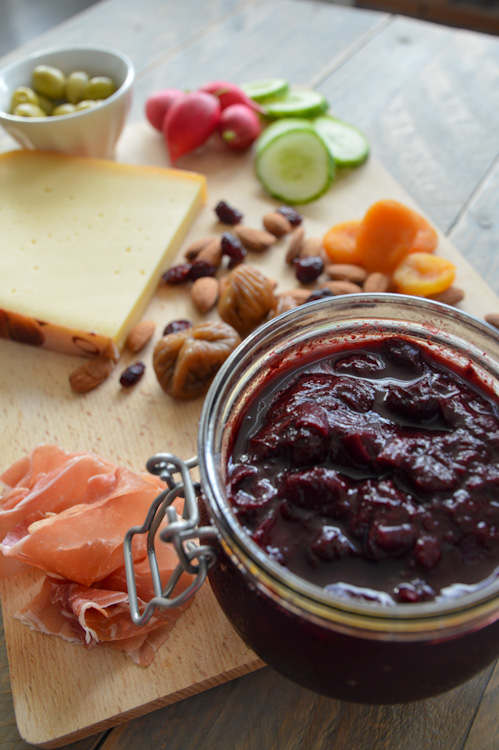 Wooden board filled with sliced meats, blocks of cheese, nuts, dried fruit, and veg. With the star - a glass jar of plum chutney on the front right corner.