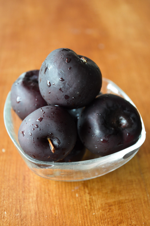 A glass bowl on a wood table holding a few dark plums - the central ingredient in our spiced plum chutney