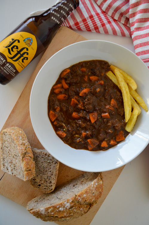 An overhead shot of a bowl of beef stew with fries (stoofvlees), bread, and a bottle of Leffe Bruin (Belgian brown ale)