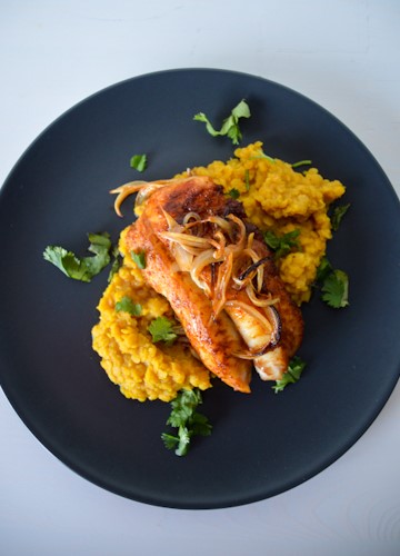 Cod cooked in a red curry paste marinade on top yellow colored red lentils, topped with onions and showered with cilantro