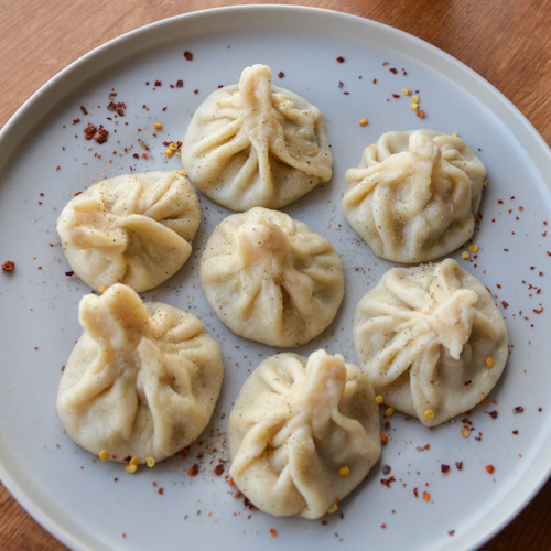 Grey plate with 7 cooked khinkali sprinkled with black pepper and red chili flake