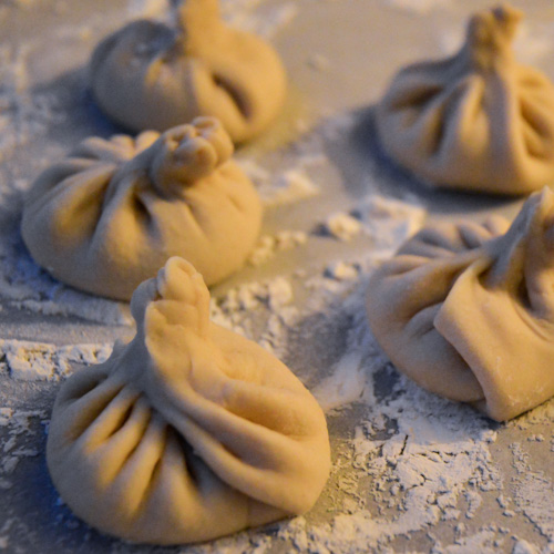 Close up of 5 Georgian dumplings (khinkali) on a floured, parchment-lined sheet pan