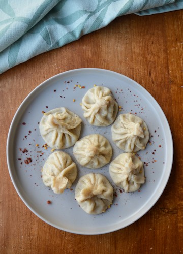 7 khinkali on a grey plate on a wood table with a green tea towel at the top