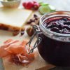 Glass jar of spiced plum chutney half out of frame along with a board of meats and cheeses