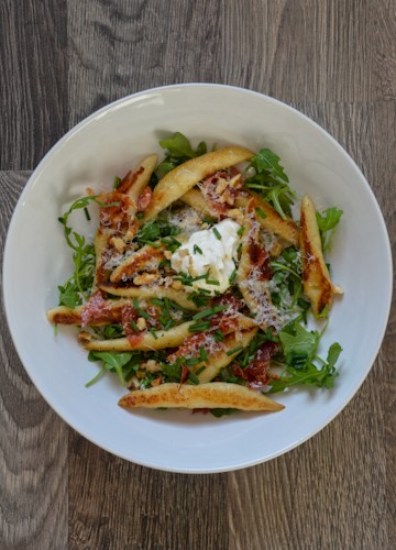 White bowl full of Shupfnudeln (German potato dumplings) plus arugula and other tasty toppings