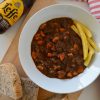 Flat lay image of a bowl of stoofvlees, bread, and a bottle of beer