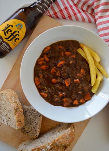 Flat lay image of a bowl of stoofvlees, bread, and a bottle of beer