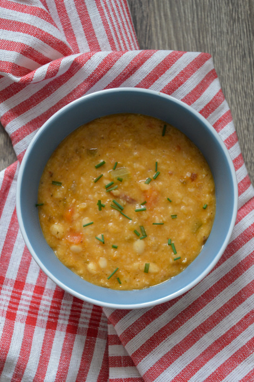 A great vegan soup recipe: a bowl of orange colored vegan white bean soup sitting on top of a red and white striped tea towel