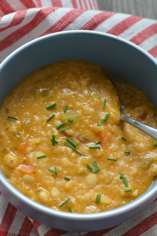 Close up of a bowl of vegan white bean soup, speckled with chives. A spoon is already digging in.