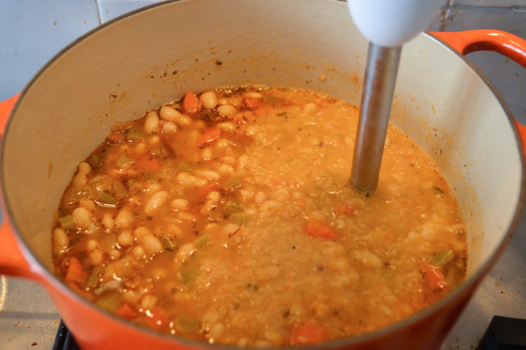 The process of blending vegan white bean soup with a stick blender