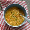 Vegan white bean soup in a bowl, with a spoon, on a red and white tea towel