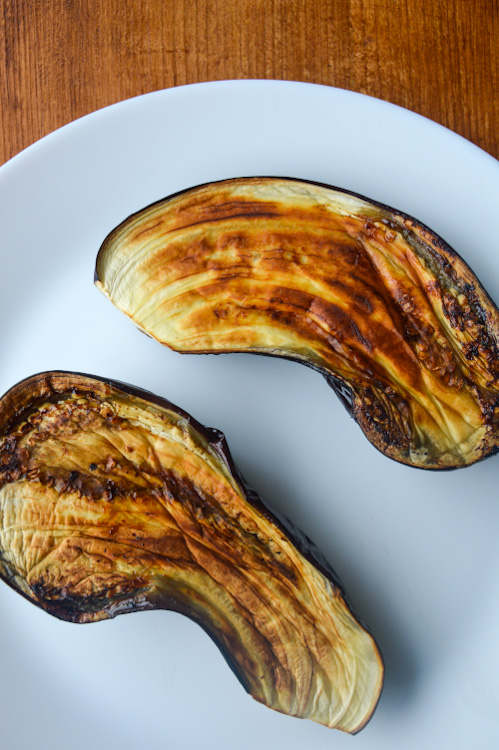 A white plate with two halves of roasted eggplant, nicely charred, face up