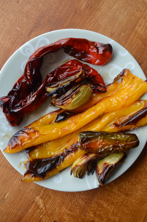 White plate holding charred, roasted red peppers, yellow peppers, onions, and jalapeno