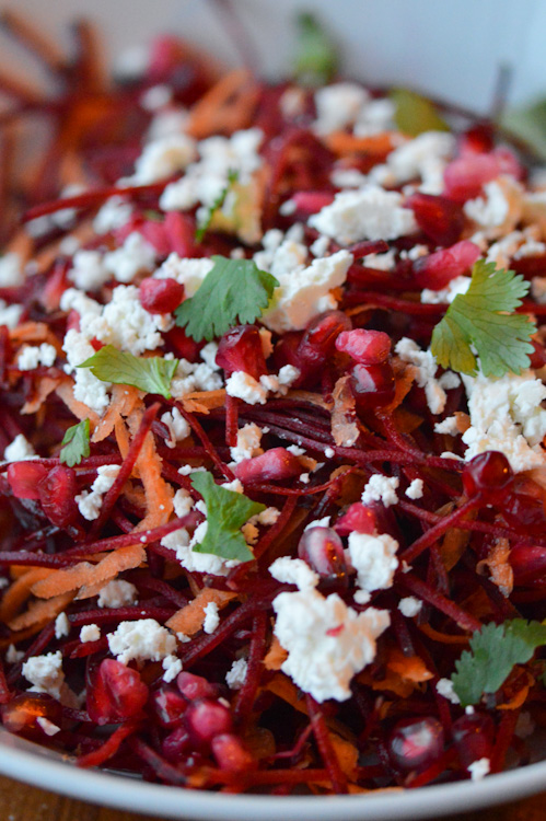 Close up of bowl of beetroot salad with feta, carrots, pomegranate seeds, and parsley