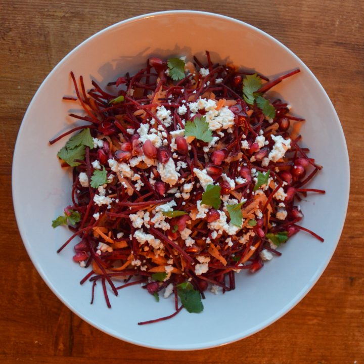 Julienned beetroot and feta salad, topped with pomegranate seeds and fresh parsley, in a white bowl