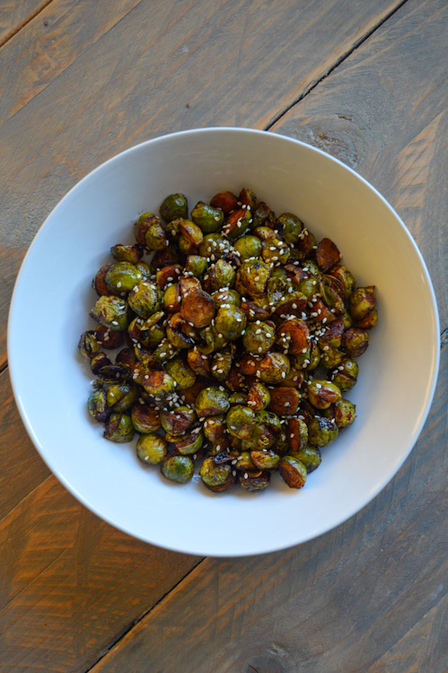A white bowl full of hoisin roasted Brussels sprouts sprinkled with sesame seeds