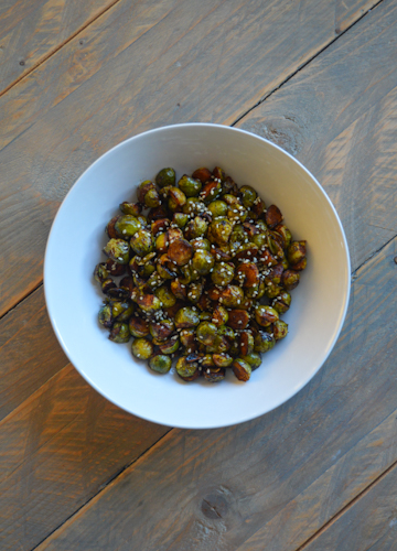 A white bowl of roasted Brussels sprouts sitting atop a wooden table