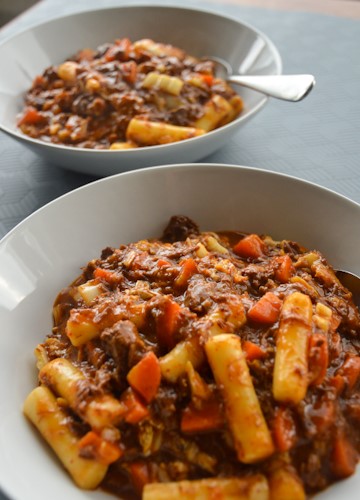 Two bowls of Korean beef stew with tubular rice cakes and carrots, one clear in the foreground, one a bit blurred in the background