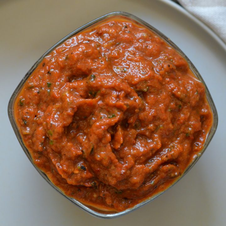 Square bowl of roasted red pepper and zucchini spread (ajvar) on a beige plate