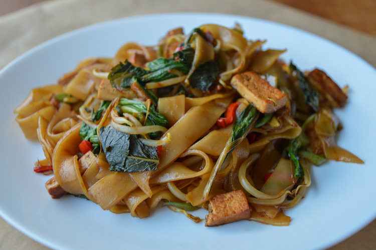 A white plate with a pile of vegetarian drunken noodles with tofu