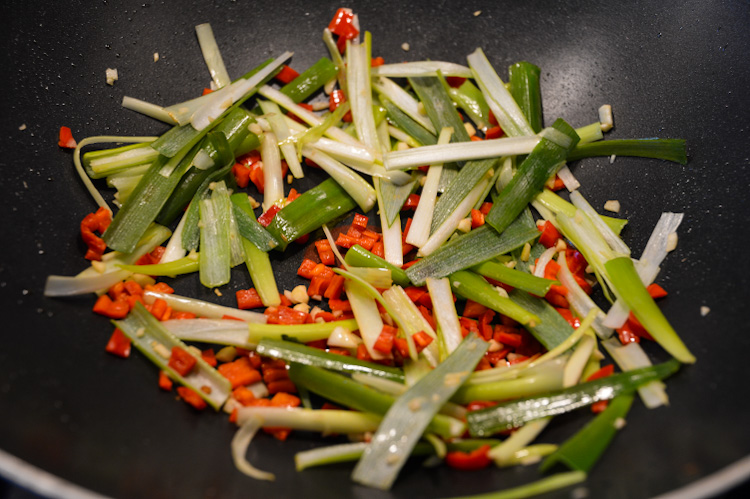 A black wok with julienned scallions and small diced hot red peppers - veg for vegan pad kee mao