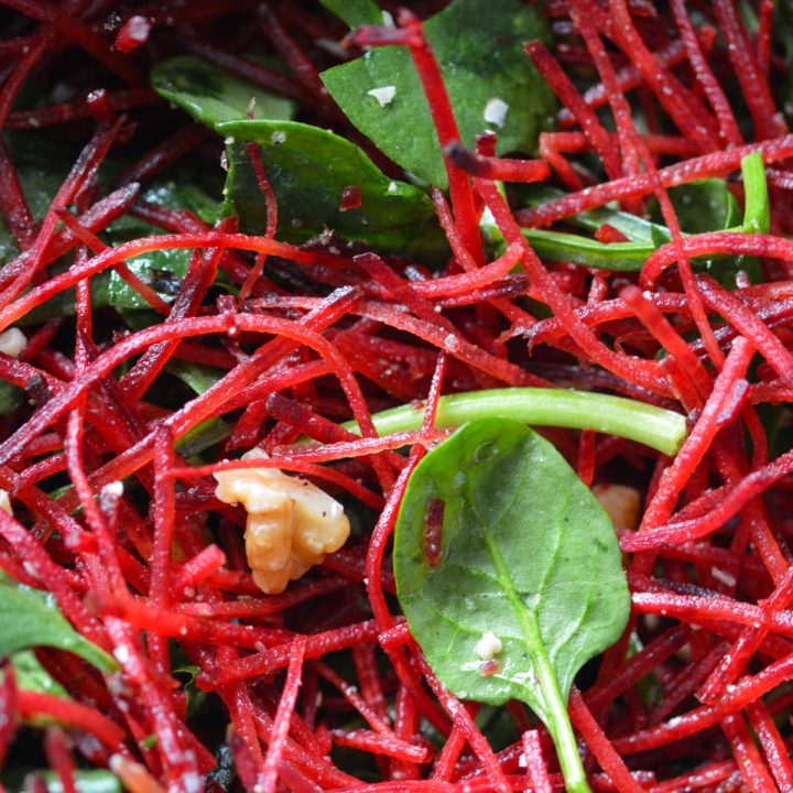 Close up shot of a salad of shredded beets, a few spinach leaves, and chopped walnuts