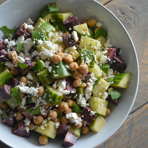 Close up of a white bowl of carrot cucumber salad with maple tahini dressing. Also in the salad: chickpeas, feta, and cilantro. Yum!