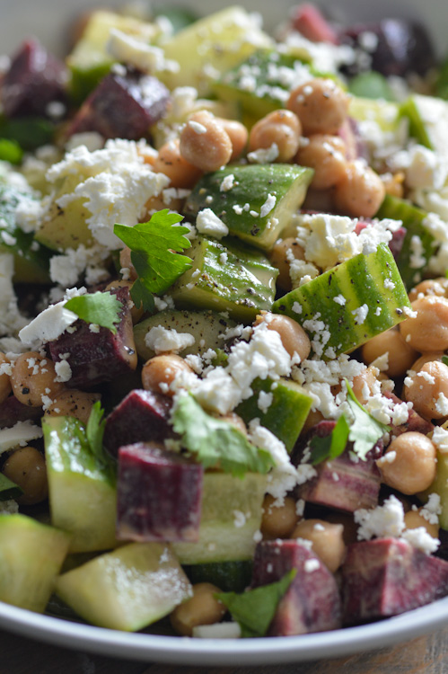 Super close up of a carrot cucumber salad (note, the carrots are purple!). It's tossed with a maple tahini dressing, but you can't really see that. You can see chickpeas, feta, and cilantro.