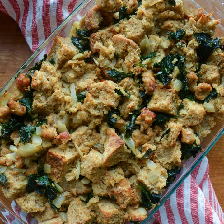 Close up of a small tray of sausage kale stuffing; tray is resting on a red and white tea towel