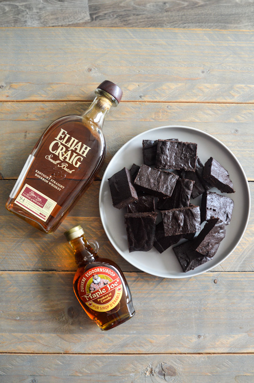 Plate of bourbon maple brownies laying next to bottles of bourbon and maple syrup on a wooden table