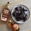 Plate of bourbon brownies laying next to bottles of bourbon and maple syrup on a wooden table