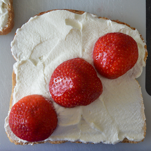 One piece of bread covered in whipped cream, with 3 strawberries running diagonally from bottom left corner to top right corner