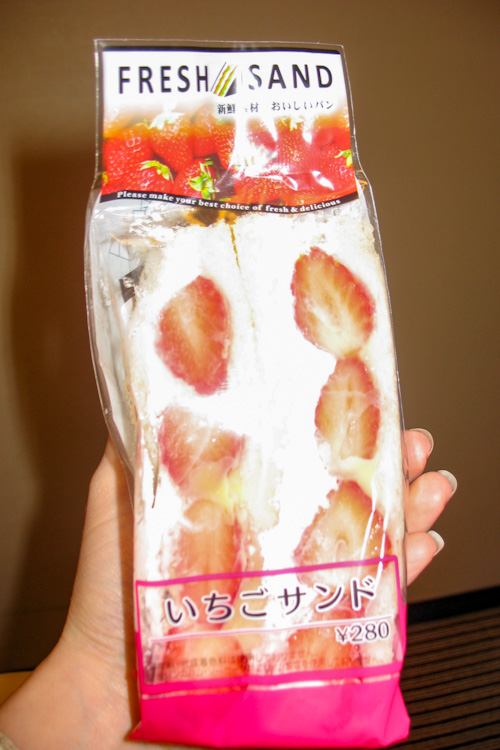 A white hand holding a strawberry sando purchased at a Japanese konbini in Tokyo; the packaging says "fresh sand"