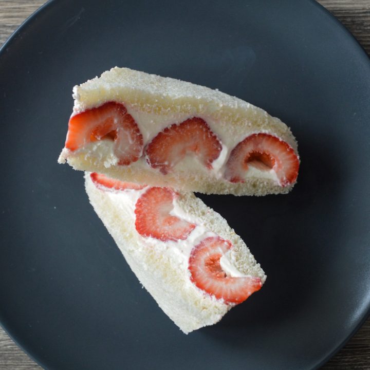 Two cut pieces of a fruit sandwich Japanese style (aka Strawberry sando) on a black plate