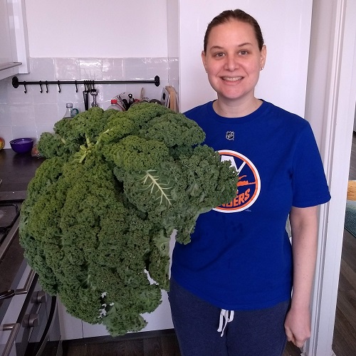 Sarah (a woman) holding an enormous bunch of kale that is almost as large as her torso